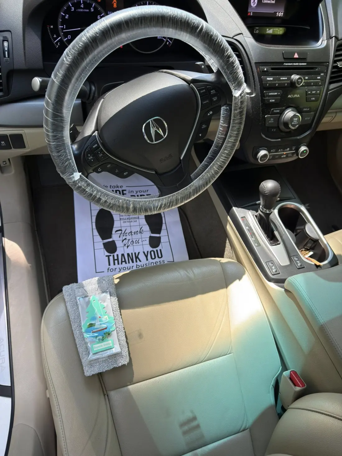 Acura interior with steering wheel cover, floor mat, and complimentary air freshener after detail